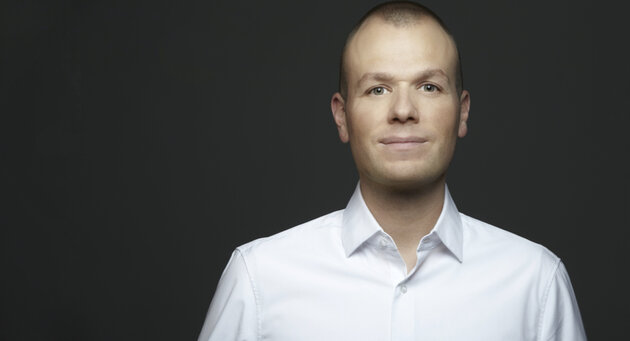 Florian Schütz in a white shirt smiles into the camera
